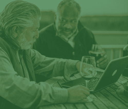 Two men looking at a laptop drinking glass of wine